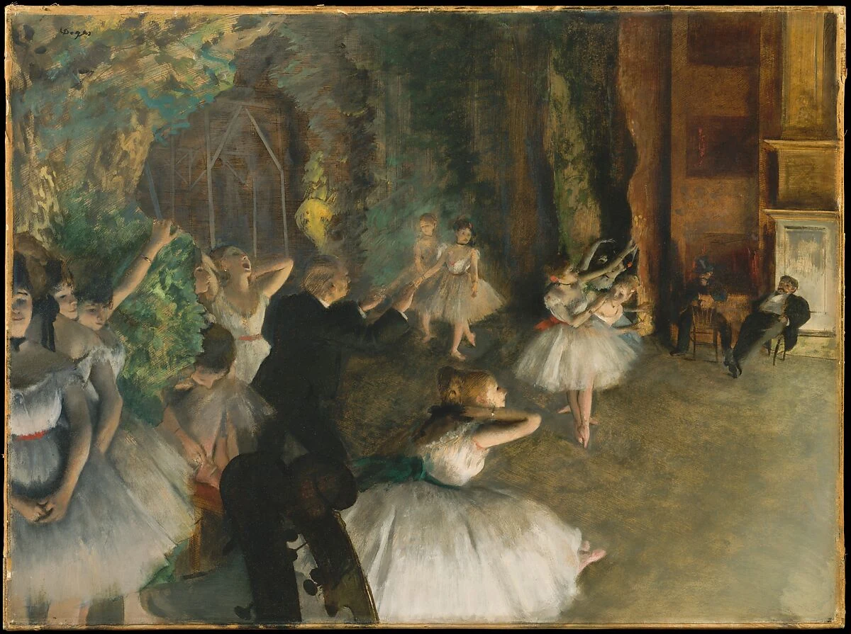 Dancers rehearse, stretch, and wait on a dim stage while two seated men watch from the right.